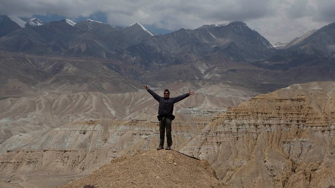 A trekker to Mustant gestures his experience amidst the backdrop of Himalayan peaks. 